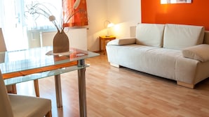 A modern living room with a glass dining table, a white sofa, and a red accent wall. - Waldpension Schiefling am See (Schiefling am See)