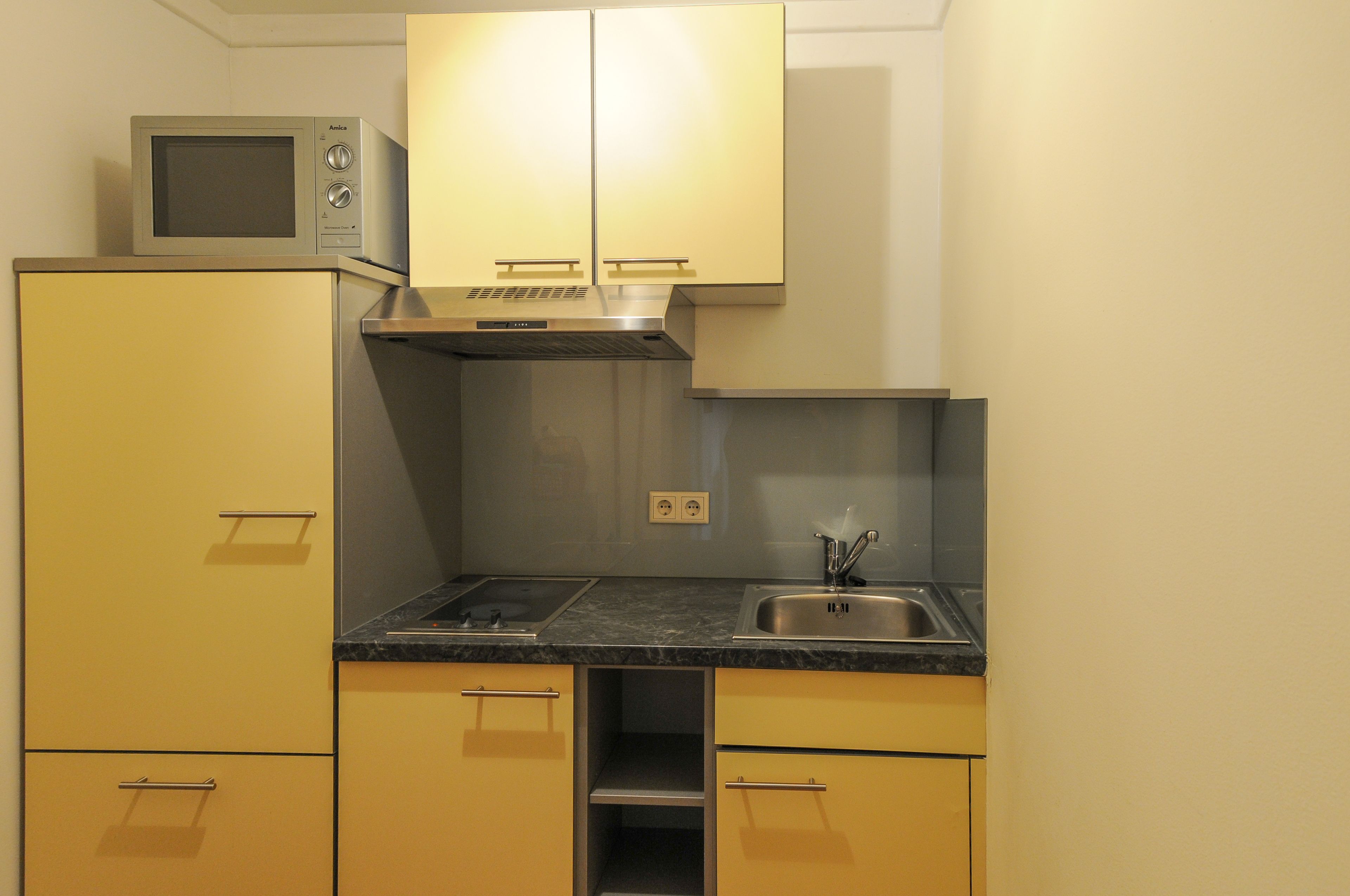 A compact kitchen with yellow cabinets, a built-in microwave, a stainless steel sink, and a gas stove.