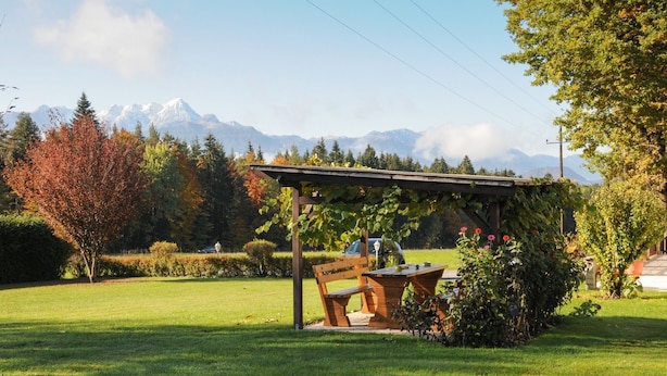 A picnic area with a wooden bench and table, surrounded by greenery and a mountain backdrop. - Waldpension Schiefling am See (Schiefling am See)