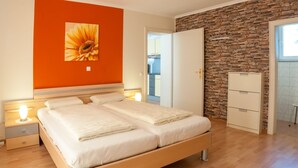 A double bed with a wooden frame, a nightstand with a lamp, a dresser with drawers, and a wall with a brick pattern. - Waldpension Schiefling am See (Schiefling am See)