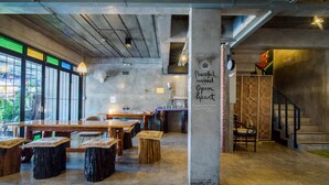 Een ruime café met houten tafels en stoelen, een betonnen pilaar met inspirerende tekst, en grote ramen die natuurlijk licht doorlaten.
