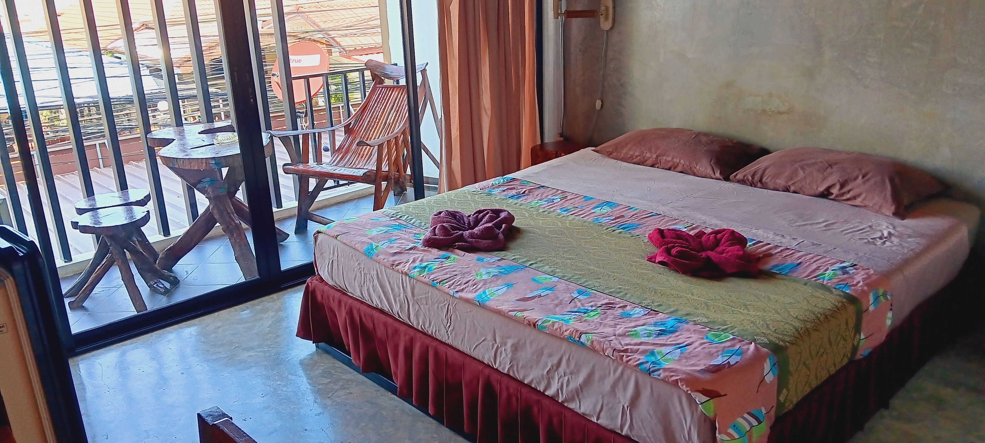 A room with a bed, a small table, a chair, and a view through a glass door.