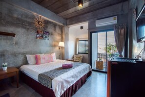 A hotel room with a bed, a desk, a lamp, a TV, and a balcony with plants. - Lovely Guesthouse 94 (Hua Hin)