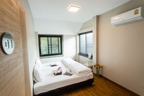 A hotel room with a bed, a window, a wall-mounted air conditioner, and a wooden floor.