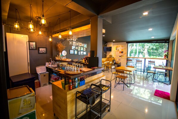 A modern bar area with a counter, stools, and hanging lights. There are framed pictures on the wall and a window with a view of trees.