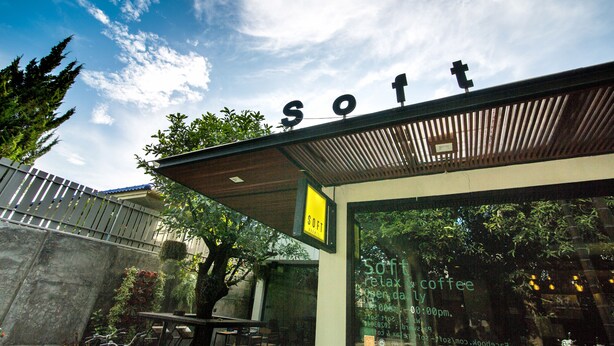 Exterior de um edifício com um letreiro que diz "SOFT" e uma placa indicando "SOFT relax & coffee" com horário de funcionamento.