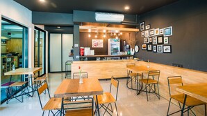 Um café moderno com mesas e cadeiras de madeira, um balcão com menu e quadros nas paredes.
