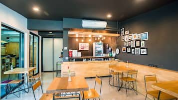 A modern cafe with wooden tables and chairs, a counter with a menu, and framed pictures on the wall.