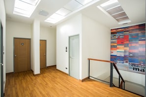 A hallway with wooden flooring, a staircase with a handrail, and a colorful abstract wall art piece.