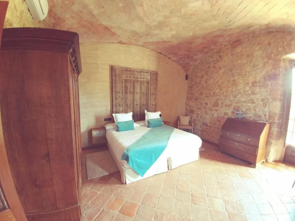 Une chambre avec un mur en pierre, une armoire en bois, un lit recouvert d’une couvre-lit bleue et blanche, et une table de chevet.