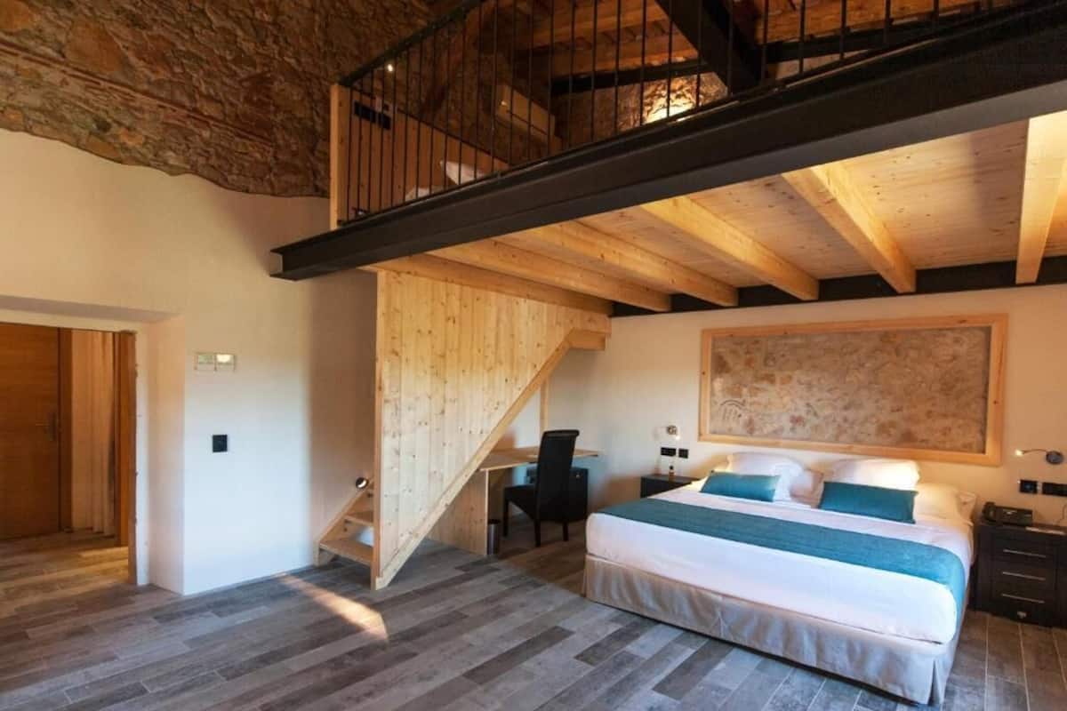 A bedroom with a large bed, a desk, and a staircase leading to an upper level.