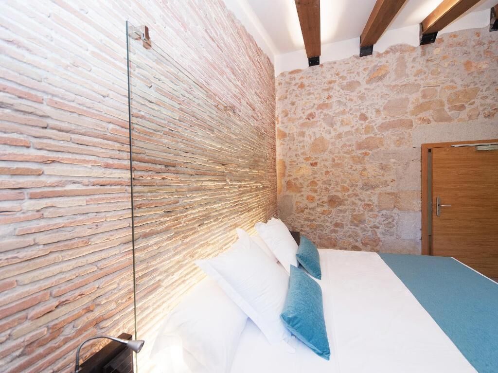 Ein Schlafzimmer mit Backsteinwand, Mauerwerk, Holzbalkendecke, einem Bett mit weißer und blauer Bettwäsche und einer Holztür.