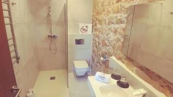 Un baño moderno con una pared de acento de piedra, ducha a ras de suelo, inodoro y tocador con espejo.