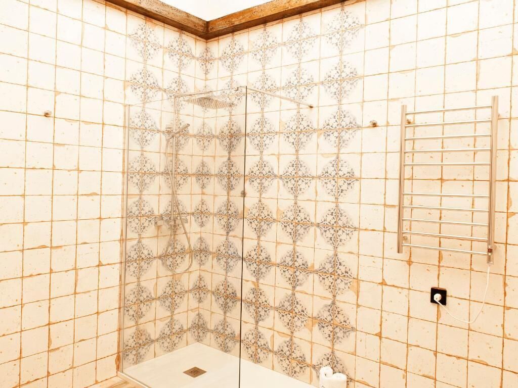 A room with a tiled shower wall, a metal rack, and a power outlet.