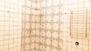 A room with a tiled shower wall, a metal rack, and a power outlet.