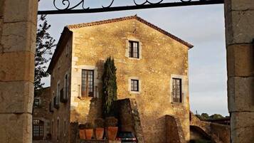 An archway with the inscription "El Moli" leading to a stone building with multiple windows and a small tree in front.