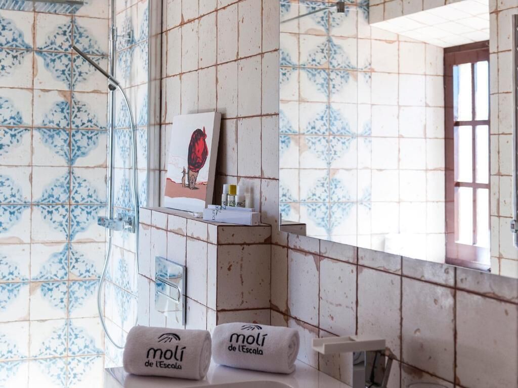 Une salle de bain avec des carreaux décorés, une douche, une serviette portant la marque « Moli de l’Escala » et un tableau encadré accroché au mur.
