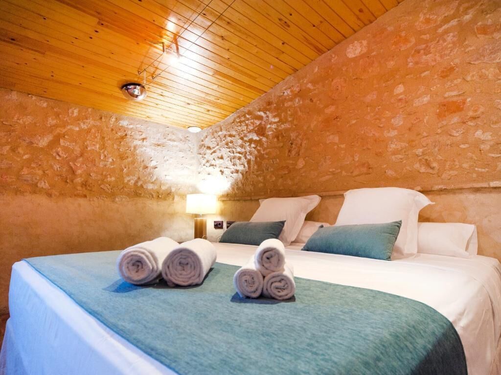 Una habitación acogedora con techo de madera, pared de piedra, cama bien hecha y toallas enrolladas, además de una lámpara en la mesita de noche.