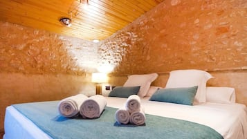 Una habitación acogedora con techo de madera, pared de piedra, cama bien hecha y toallas enrolladas, además de una lámpara en la mesita de noche.