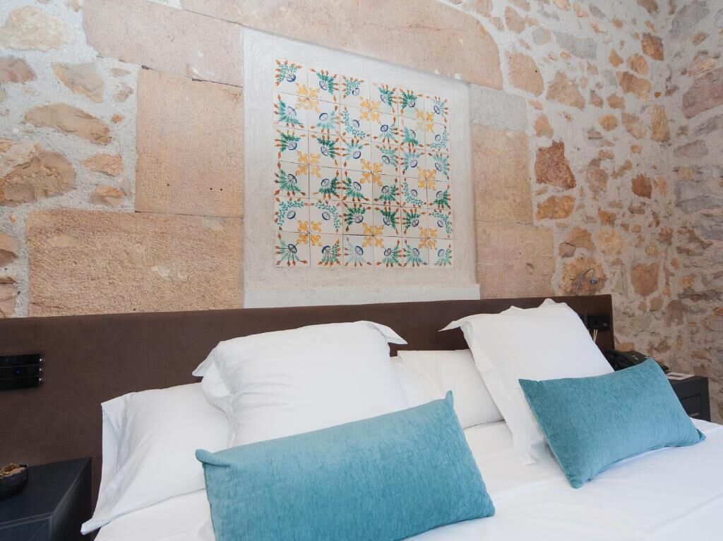 A bed with white and blue pillows, a stone wall, and a framed artwork above the bed.