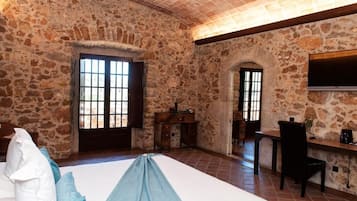 A stone-walled room with a bed, a desk, and a TV.