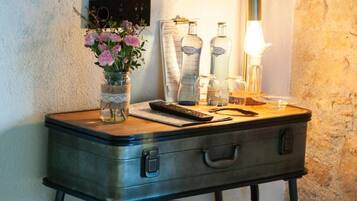 Un bureau de style vintage agrémenté d’une valise, d’un vase de fleurs, d’une lampe et de quelques bouteilles.