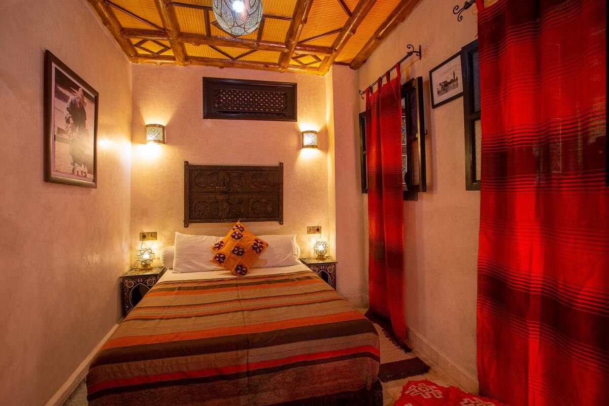 A bedroom with a bed, two bedside lamps, a wall-mounted light fixture, and a red curtain.