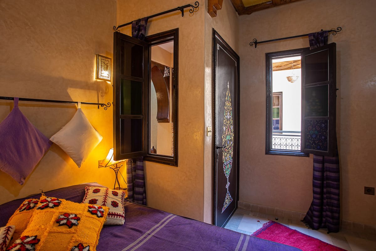 A bedroom with a bed, a window with curtains, a door, and a wall-mounted light fixture.