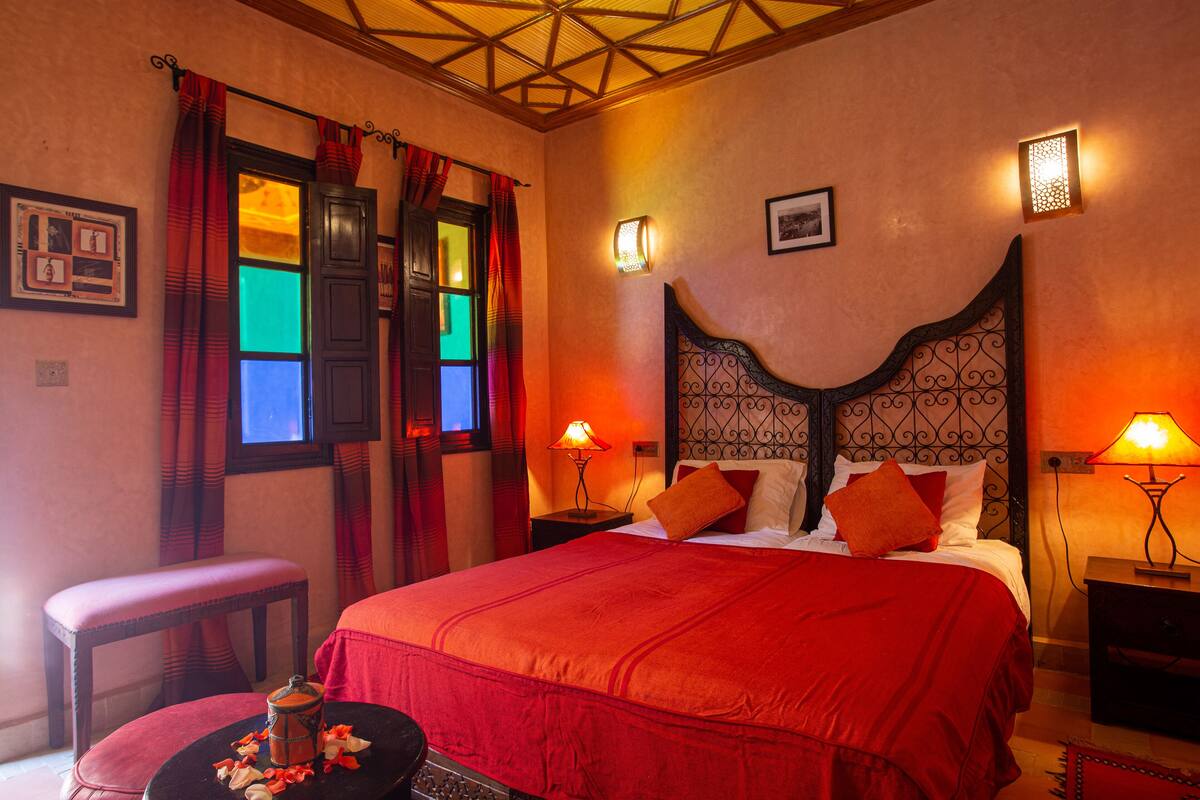 A room with a large bed, two bedside tables, a small table with a vase, and a bench.