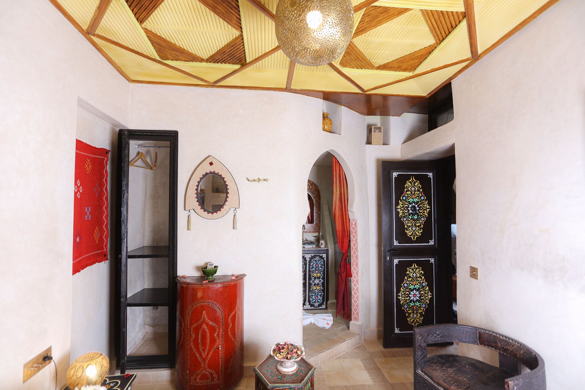 Ein traditionelles Interieur mit einer geometrischen Decke, einem Spiegel, einem roten Schrank und einer Tür mit Muster.