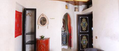 Ein traditionelles Interieur mit einer geometrischen Decke, einem Spiegel, einem roten Schrank und einer Tür mit Muster.