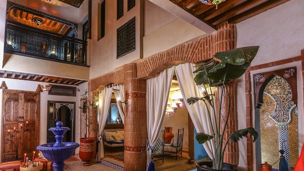 Un interno tradizionale marocchino con una fontana, piante in vaso e vista su una camera da letto.