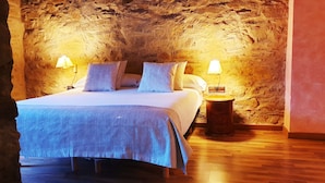A bed in a room with a stone wall, two bedside lamps, and a wooden floor. - Can Gasparó Hotel Rural & Restaurant (Planoles)
