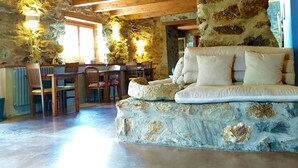A cozy interior with a stone wall, wooden ceiling beams, a sofa, and a dining area with chairs and tables. - Can Gasparó Hotel Rural & Restaurant (Planoles)