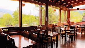 A restaurant with large windows offering a view of a forested mountain range. Tables and chairs are arranged for dining. - Can Gasparó Hotel Rural & Restaurant (Planoles)
