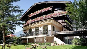 A multi-story building with balconies adorned with flowers, a covered outdoor seating area, and a mountainous backdrop. - Aparthotel Landhaus St. Joseph (Mayrhofen)