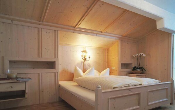 A wooden bedroom with a bed, bedside tables, and a wall-mounted lamp. - Aparthotel Landhaus St. Joseph (Mayrhofen)