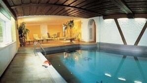 An indoor swimming pool with lounge chairs and a staircase leading to an upper level. - Aparthotel Landhaus St. Joseph (Mayrhofen)