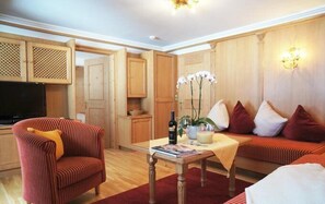 A living room with a striped armchair, a sofa, a coffee table, and a TV. There is a wooden cabinet and a wall-mounted light fixture. - Aparthotel Landhaus St. Joseph (Mayrhofen)