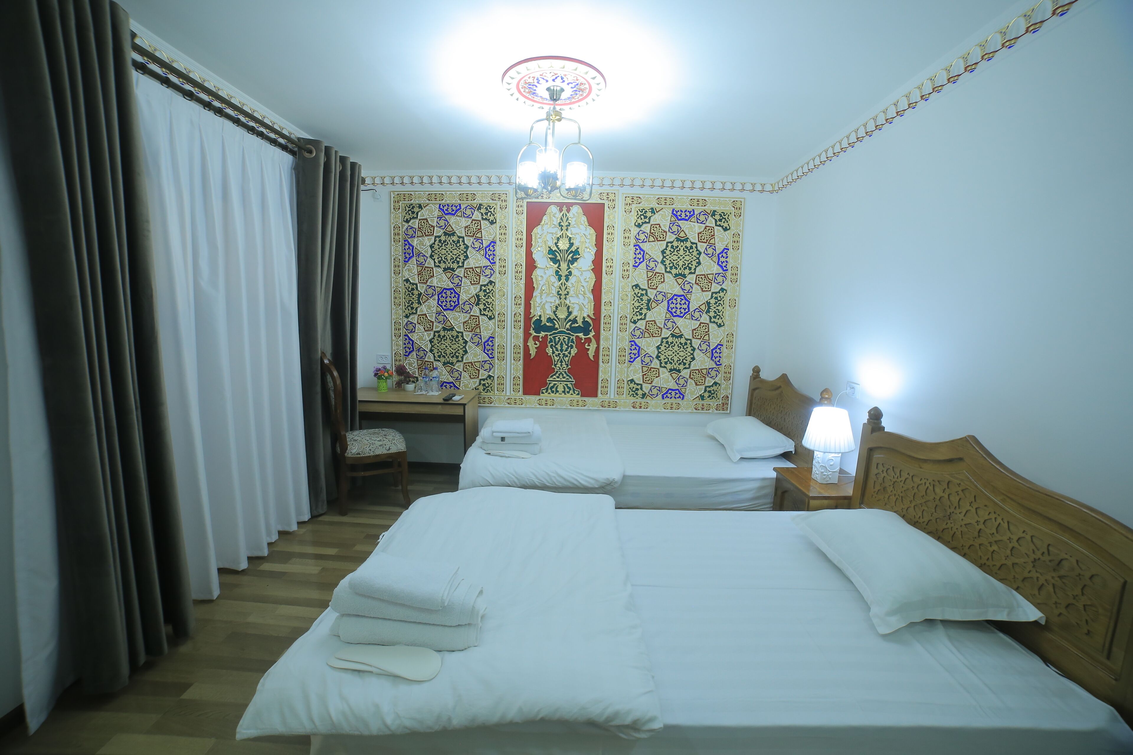 Une chambre d’hôtel avec deux lits, un bureau, une chaise, une table de chevet avec une lampe et un panneau décoratif au mur.