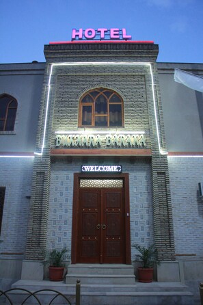 A hotel entrance with a neon sign, a welcome sign, and a wooden door. - Bukhara Baraka Hotel (Bukhara)