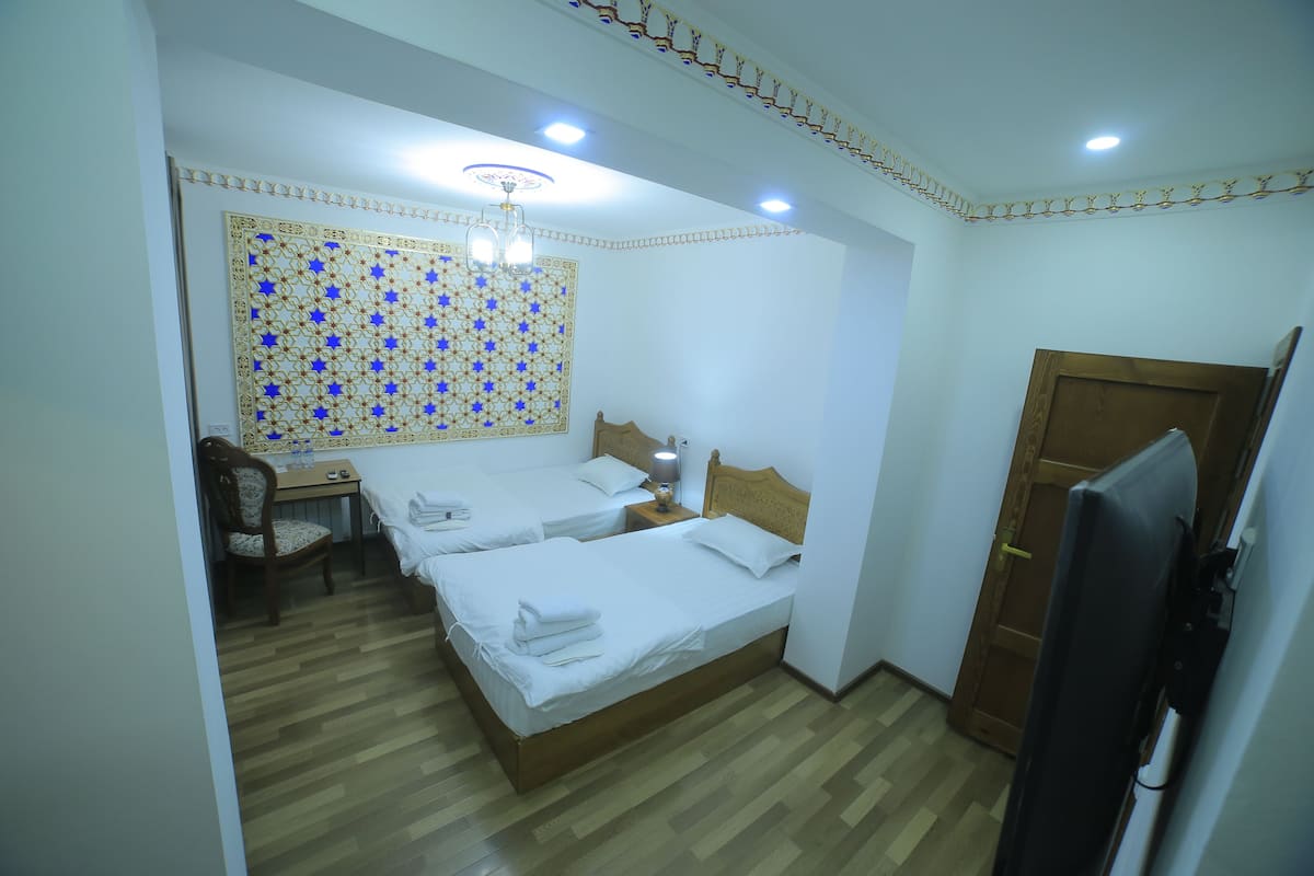 Habitación de hotel con dos camas, piso de madera, un escritorio con silla, un tapiz en la pared y una lámpara en el techo.