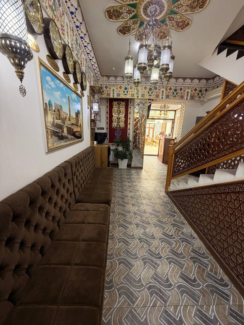 Um corredor com piso estampado, um sofá marrom, um candelabro e uma escadaria.