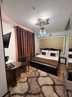 A hotel room with a bed, a desk, a chair, a television, and a decorative ceiling light. - Bukhara Baraka Hotel (Bukhara)