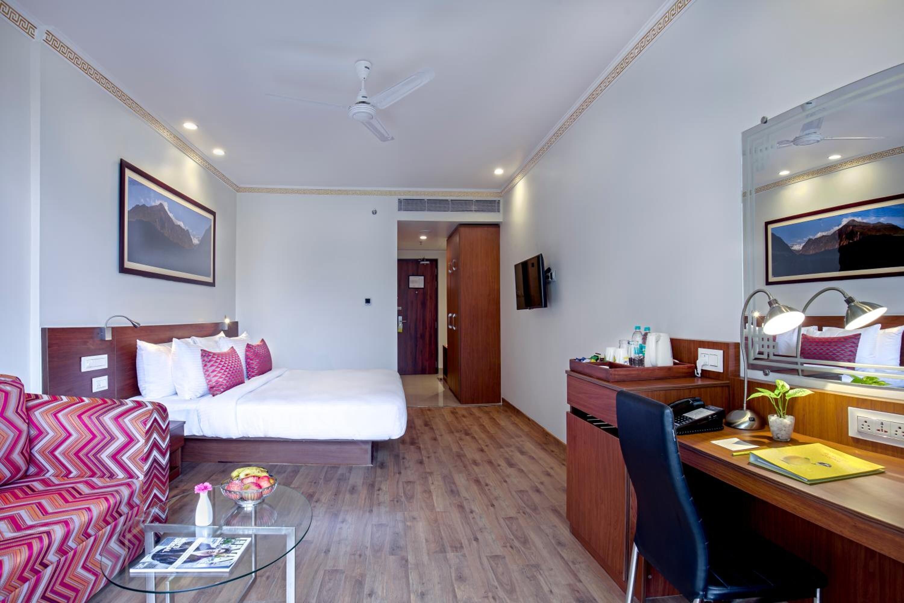 A hotel room with a bed, a desk, a chair, a coffee table, and a TV.