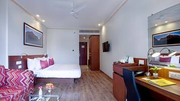 A hotel room with a bed, a desk, a chair, a coffee table, and a TV.