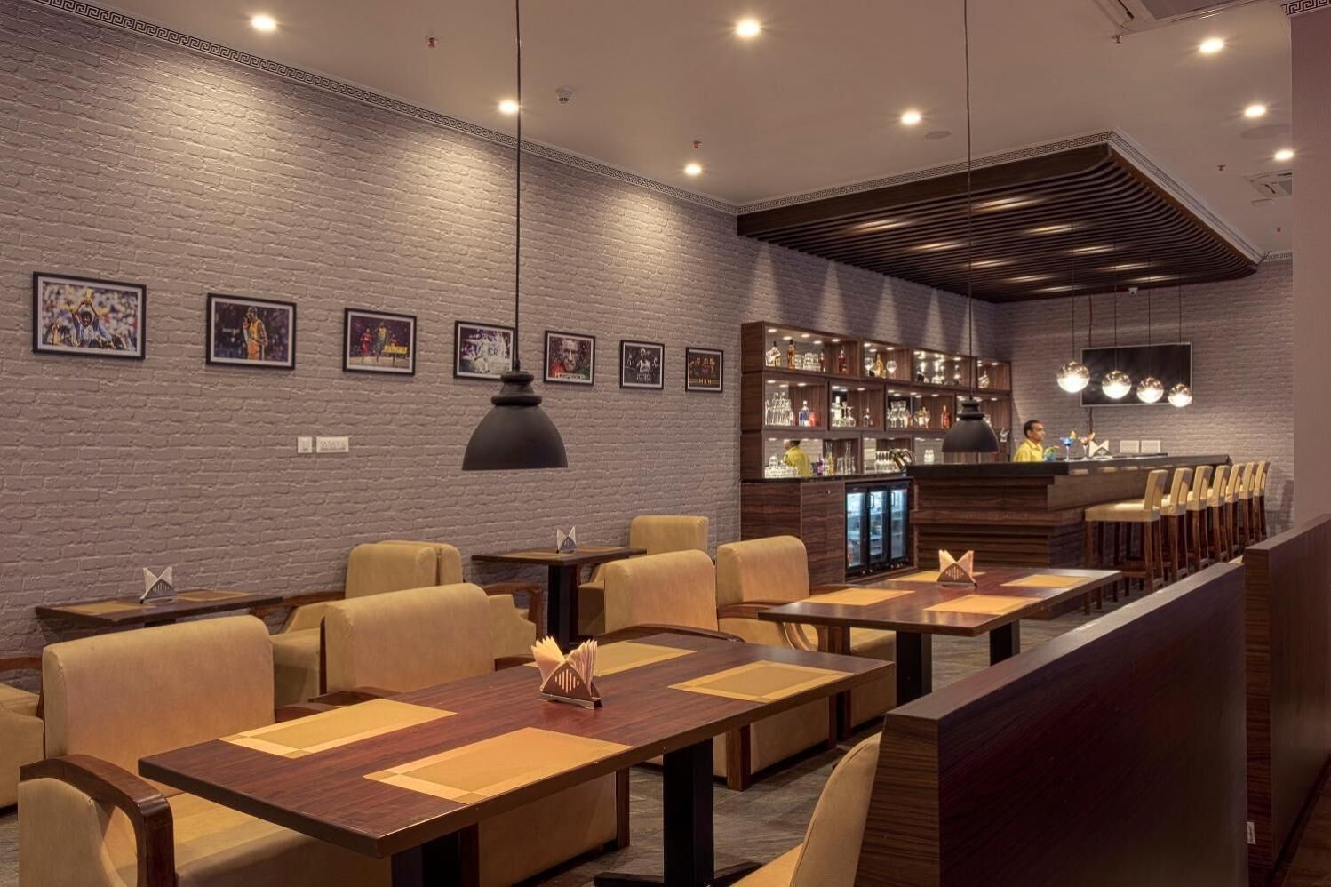Un restaurante con paredes de ladrillo, mesas y sillas de madera. Se observan cuadros enmarcados en la pared y una zona de bar con un cantinero.