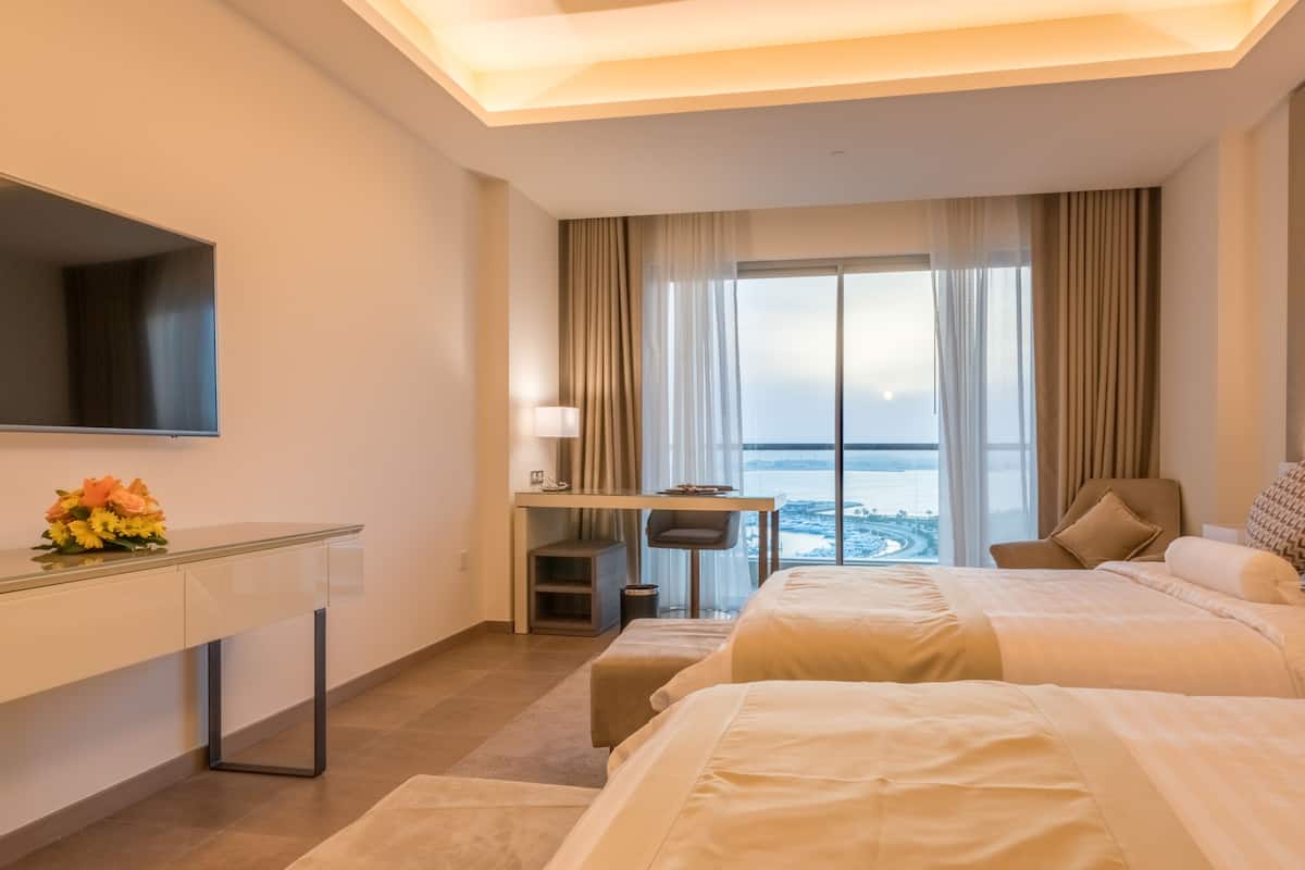 Quarto de hotel com cama, escrivaninha, cadeira, televisão e vista para o mar.