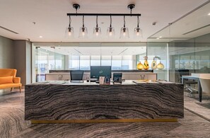 Un espacio de oficina moderno con un escritorio central tipo isla, paredes de cristal y vistas a la ciudad.