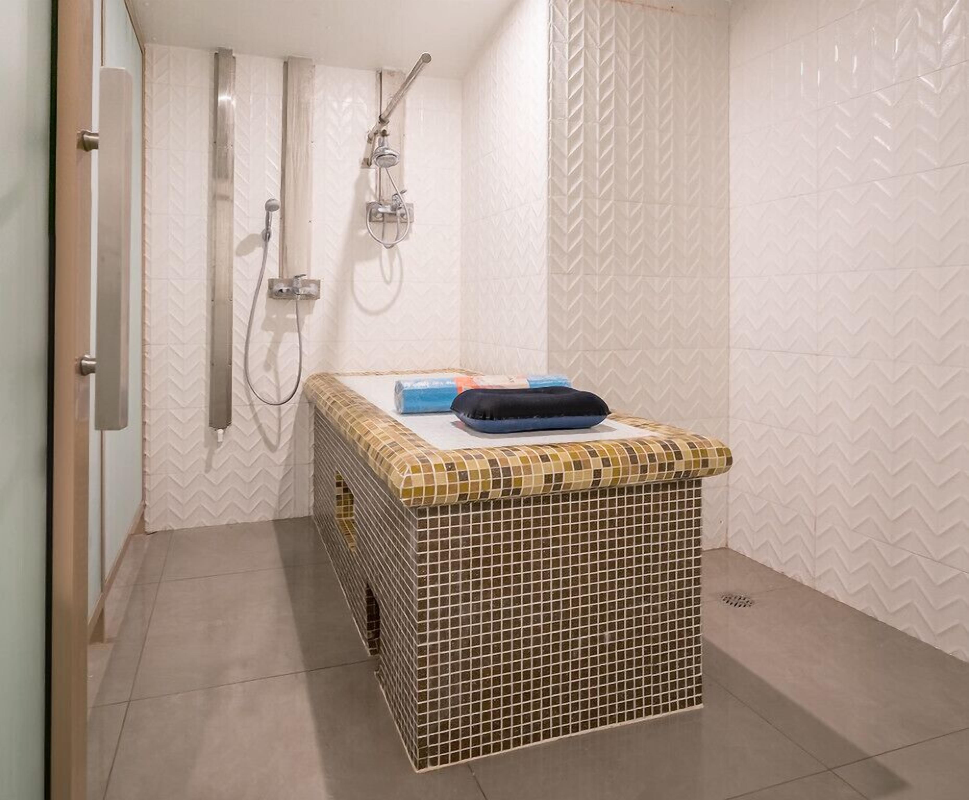 A bathroom with a tiled shower enclosure, a sink, and a small bench with towels.